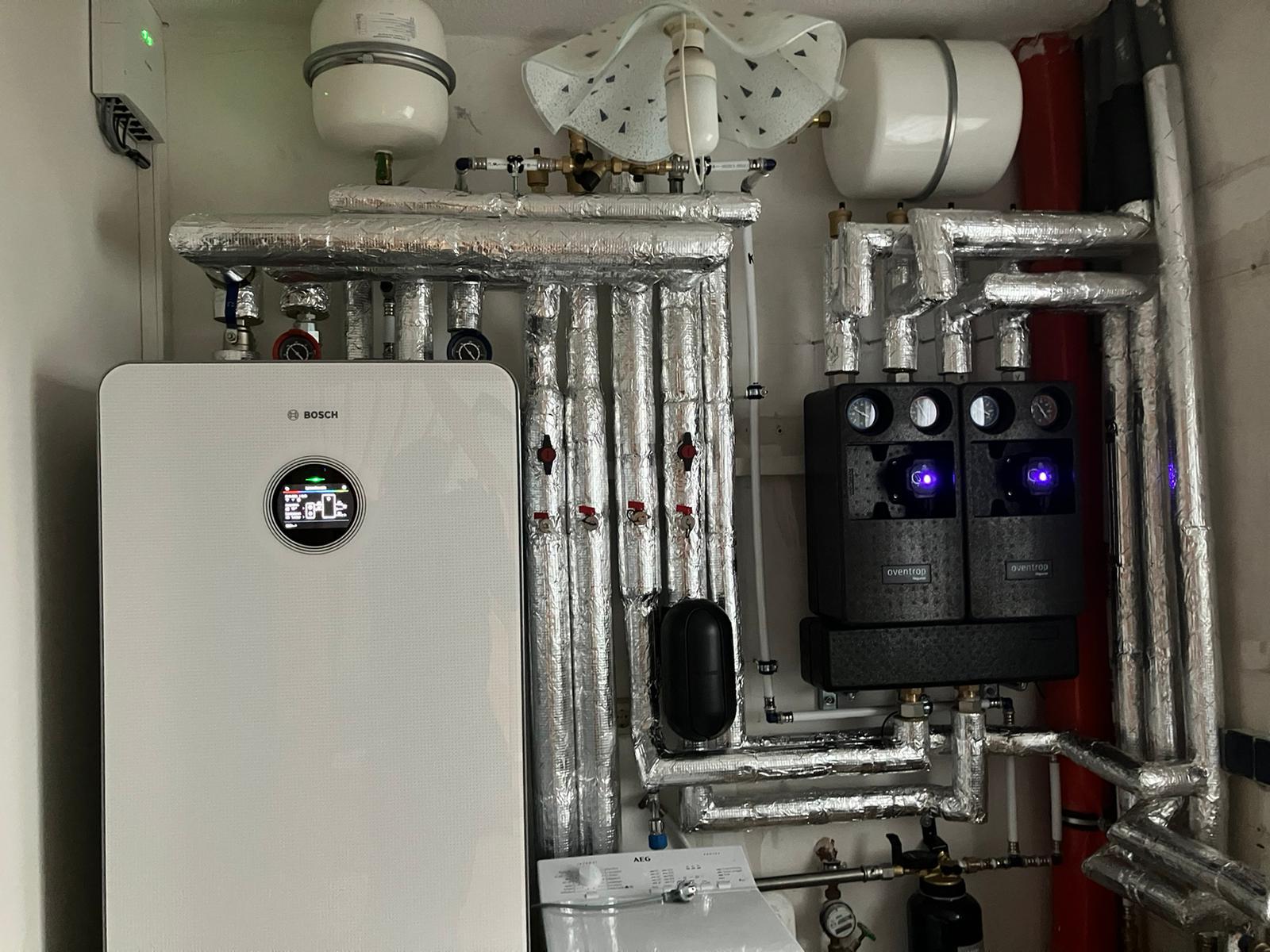 Eine komplexe Heizungsanlage mit isolierten Rohren und einem Bosch-Heizkessel in einem Technikraum.