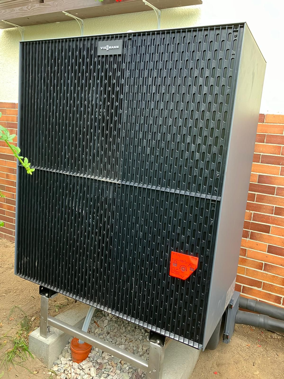 Wärmepumpe von Viessmann mit schwarzem Gitter, orangefarbene Abdeckung, Ziegelwand im Hintergrund.