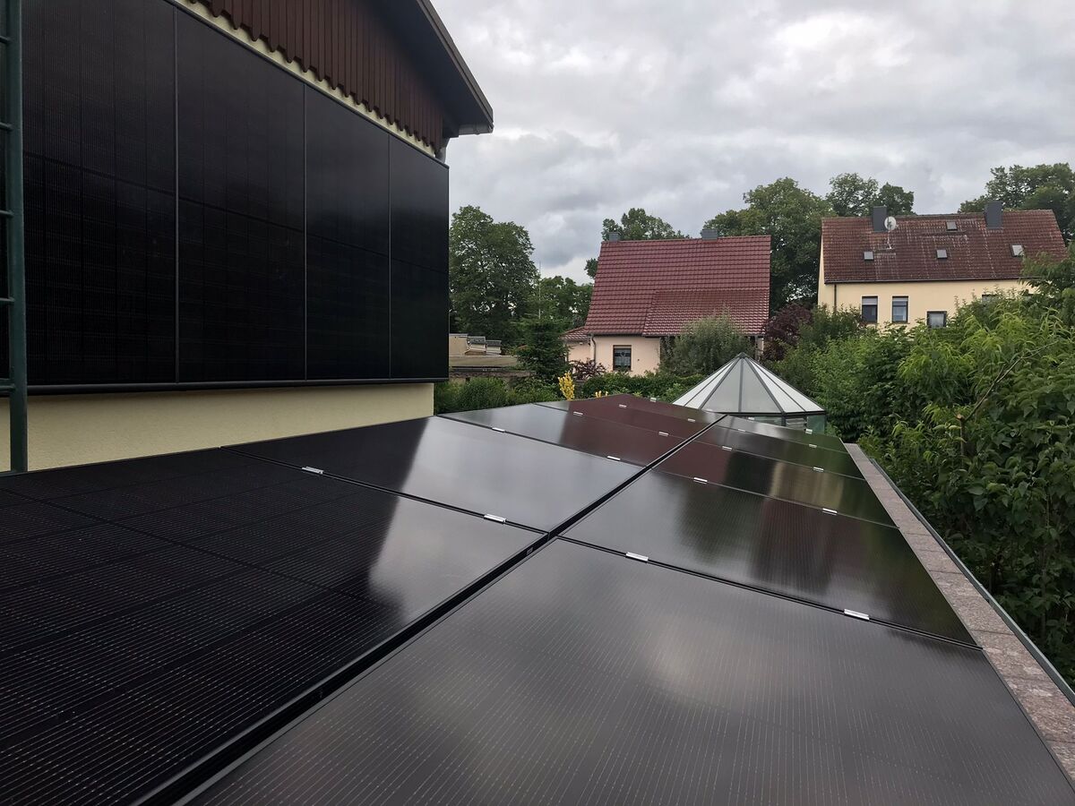 Solarpanele auf einem Dach; Himmel bewölkt; umgeben von Bäumen und Häusern mit roten Dächern.