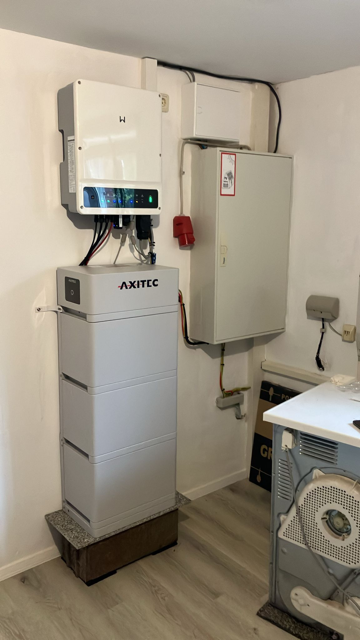 Weiße Wand mit elektrischen Geräten: Wechselrichter und Batteriespeicher in einem Technikraum.