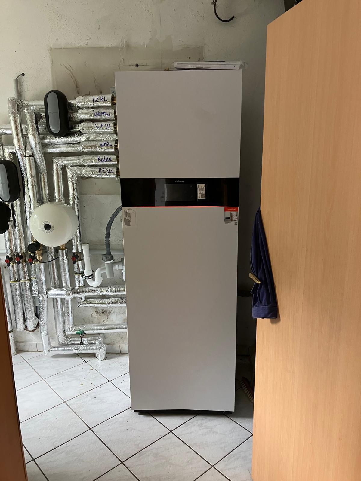 Heizung in einem Technikraum mit weißen Rohren und Fliesen; sauber und gut organisiert.