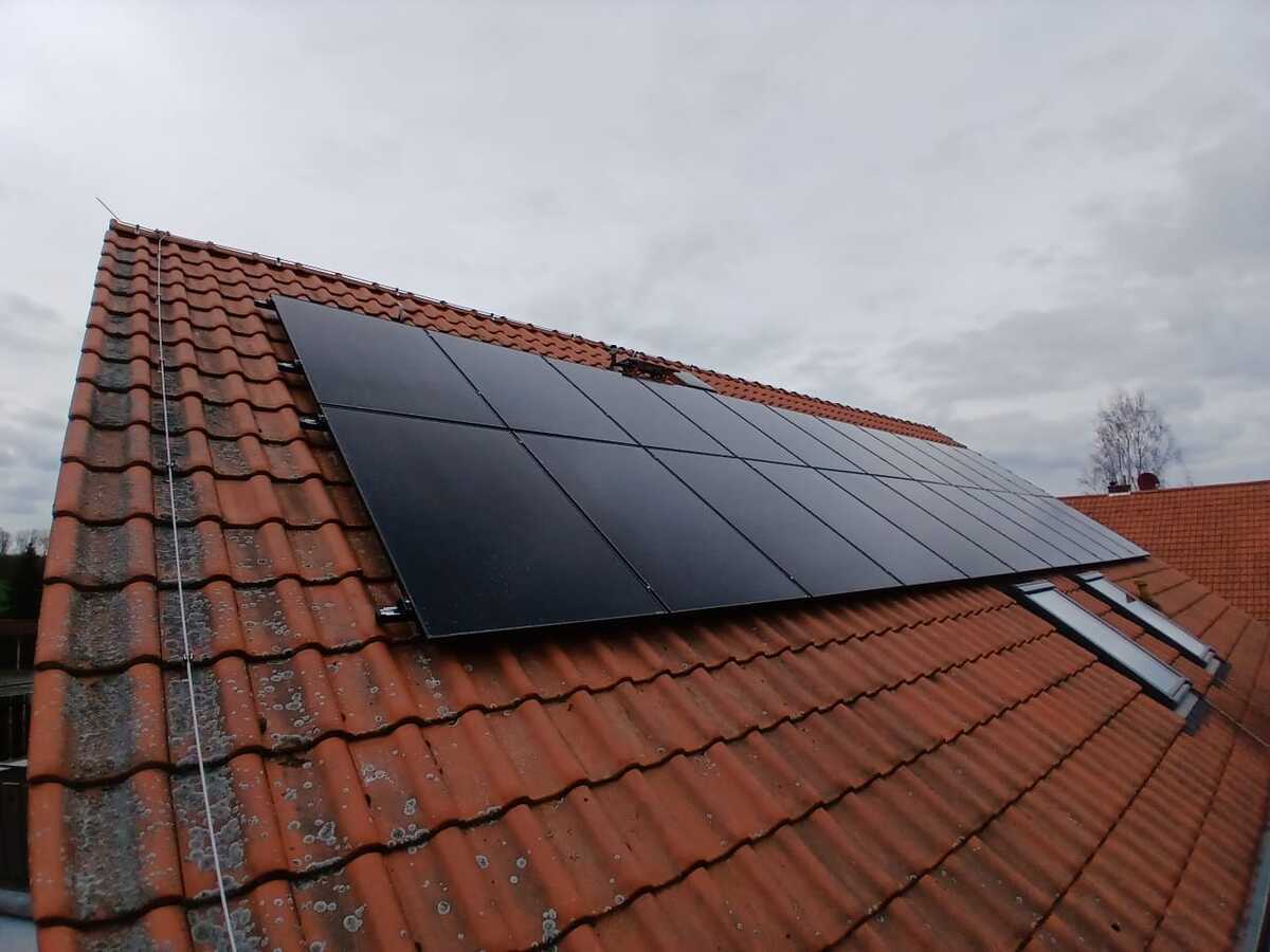 Eine Solaranlage auf einem roten Ziegeldach unter bewölktem Himmel.