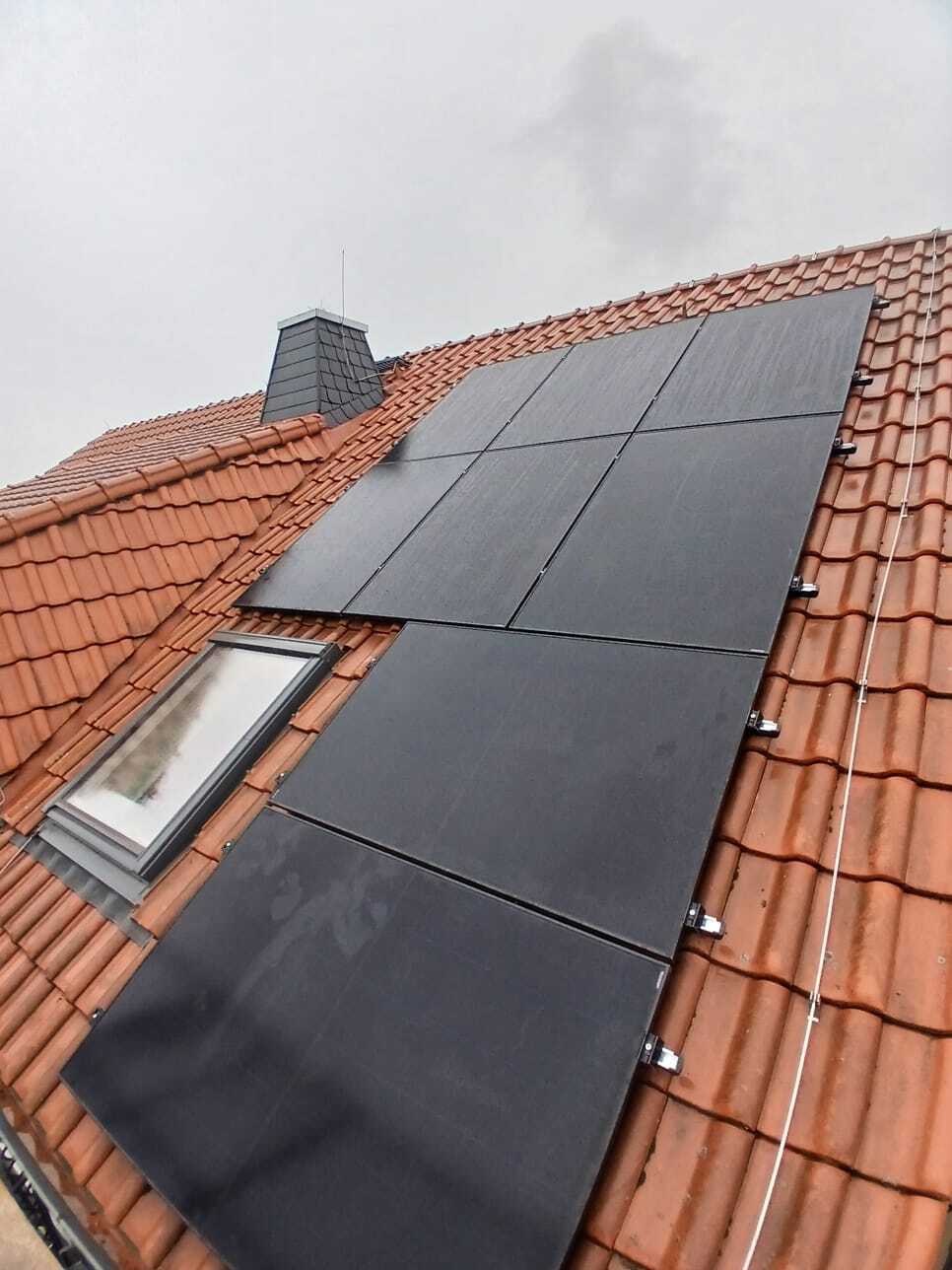 Ein Ziegeldach mit schwarzen Solarpaneelen unter grauem Himmel in einem Wohngebiet.