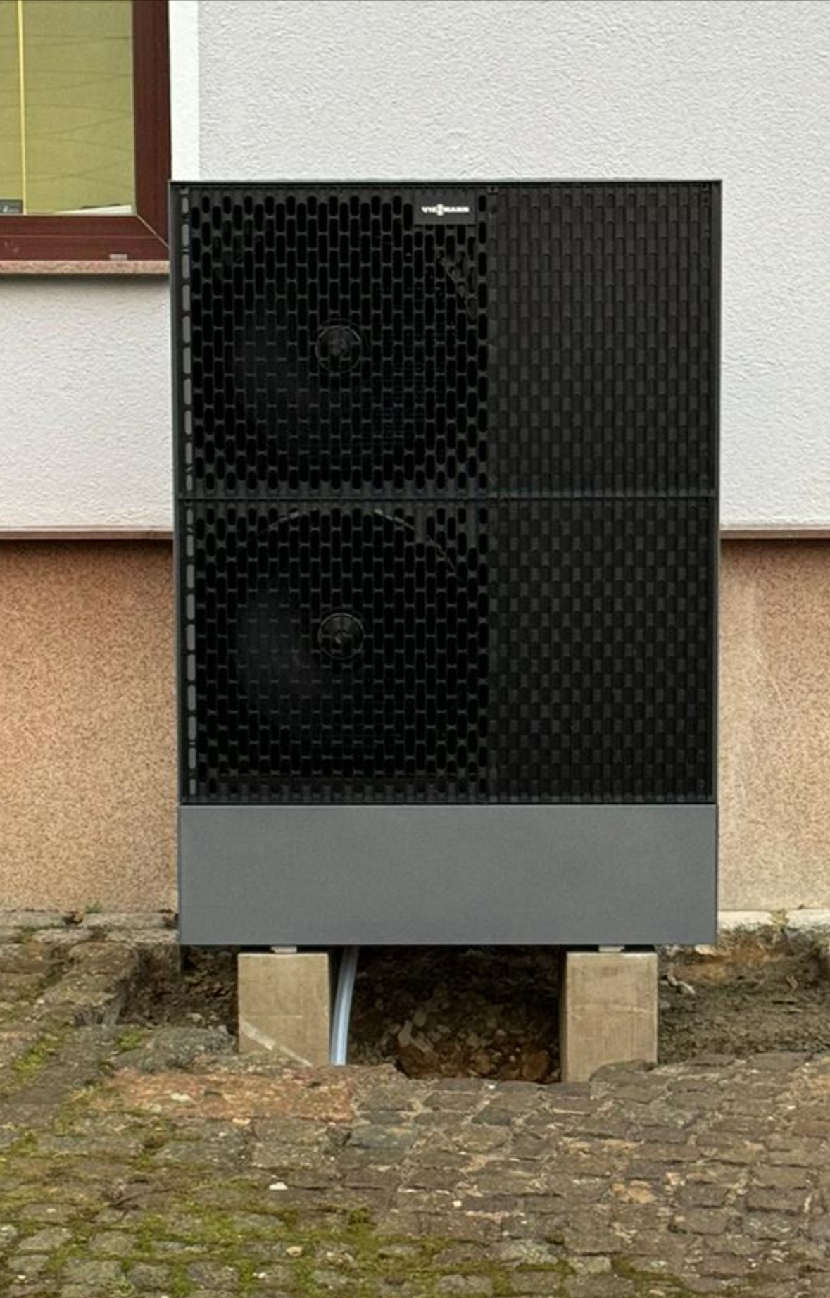 Außen-Wärmepumpe an Gebäude mittlerer Größe, schwarz-graues Gehäuse mit zwei Lüftern.