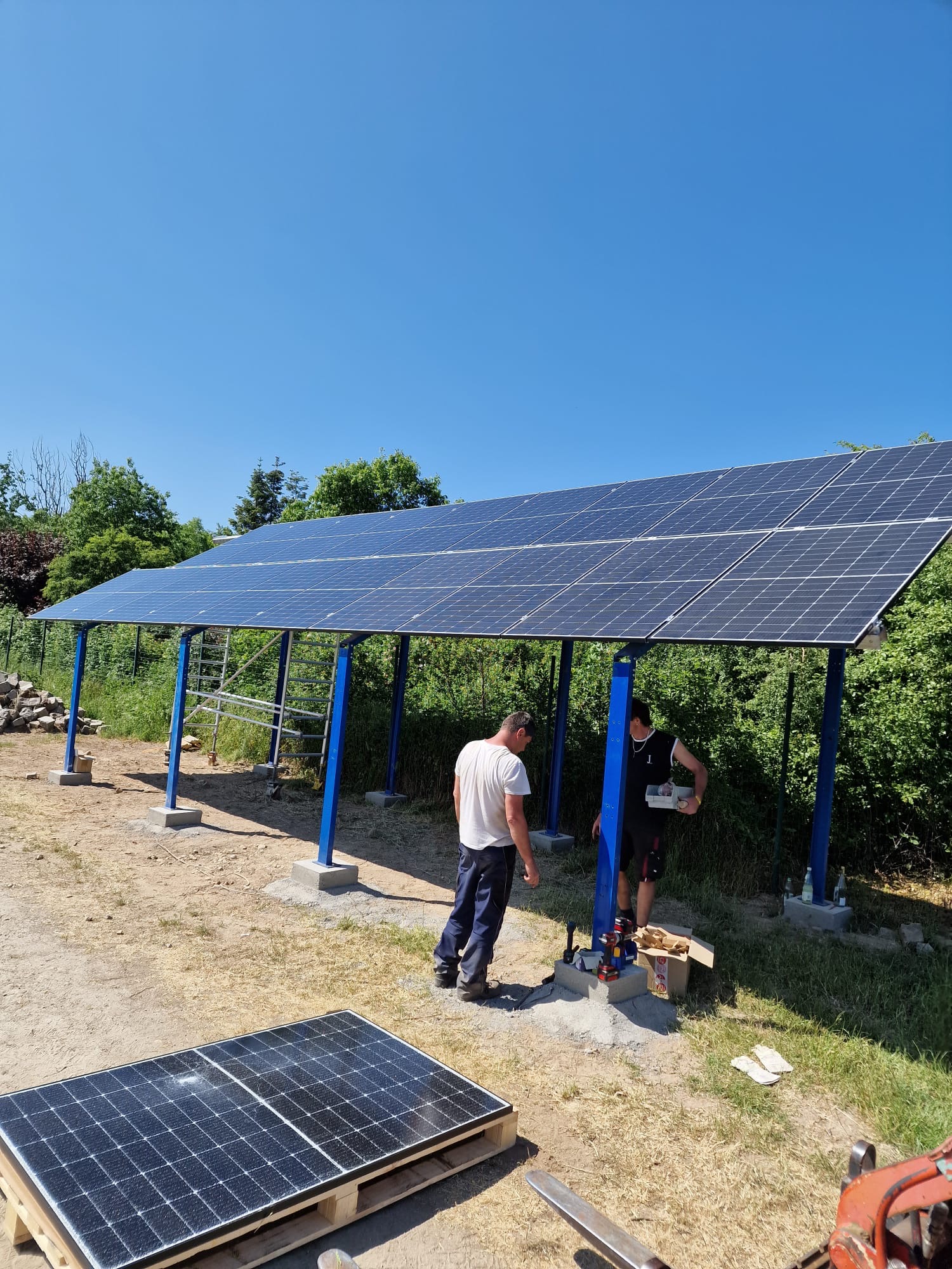 Zwei Personen installieren fröhlich Solarzellen auf einer blauen Stahlkonstruktion im Freien.