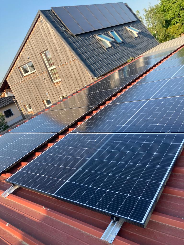 Solarzellen auf einem Hausdach, modernes Design, strahlend blauer Himmel im Hintergrund.