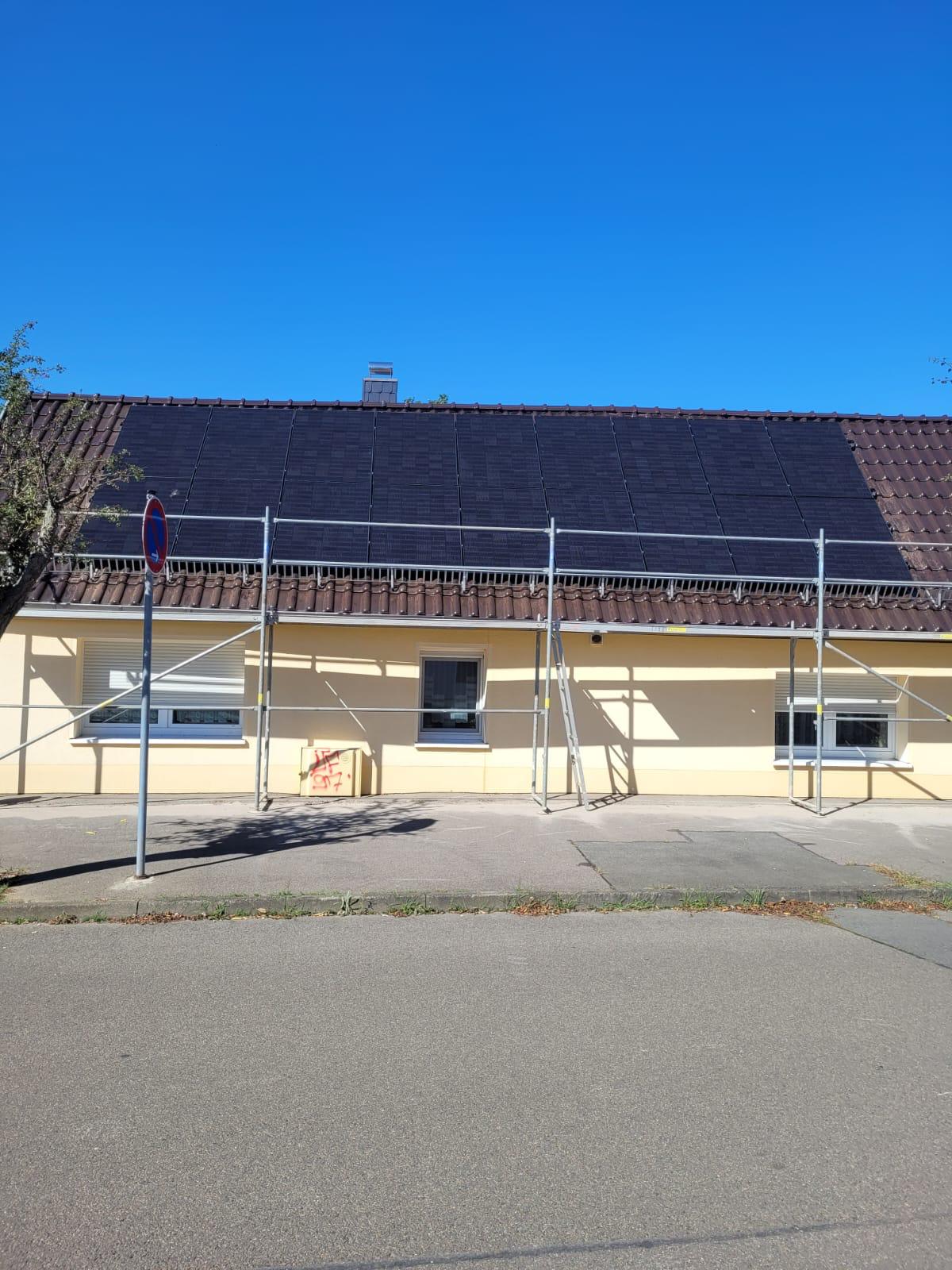 Ein gelbes Haus mit Solarpanels auf dem Dach und einem Baugerüst davor.