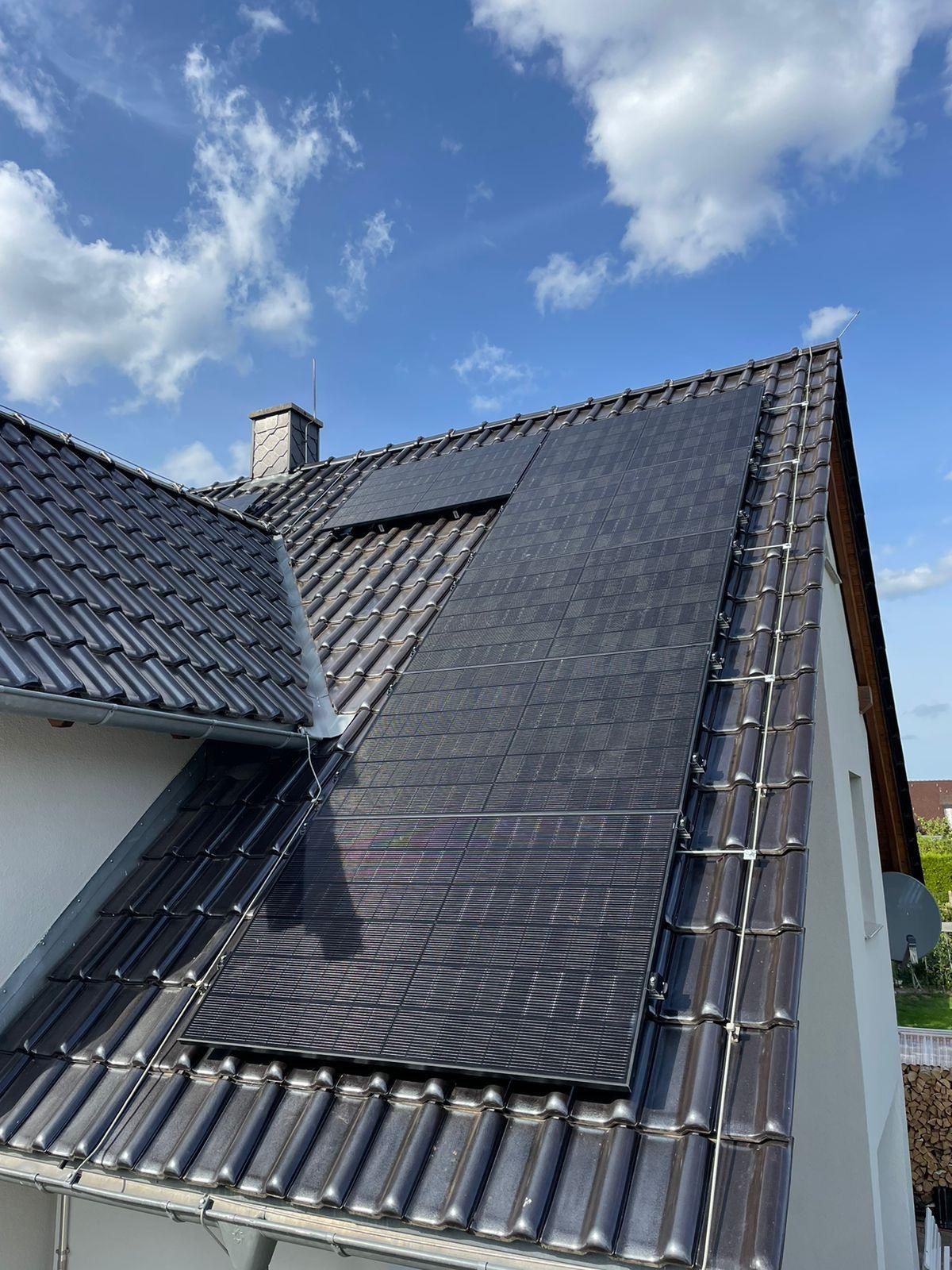 Dach mit solaren schwarz-grauen Fotovoltaikpaneelen, blauer Himmel im Hintergrund.