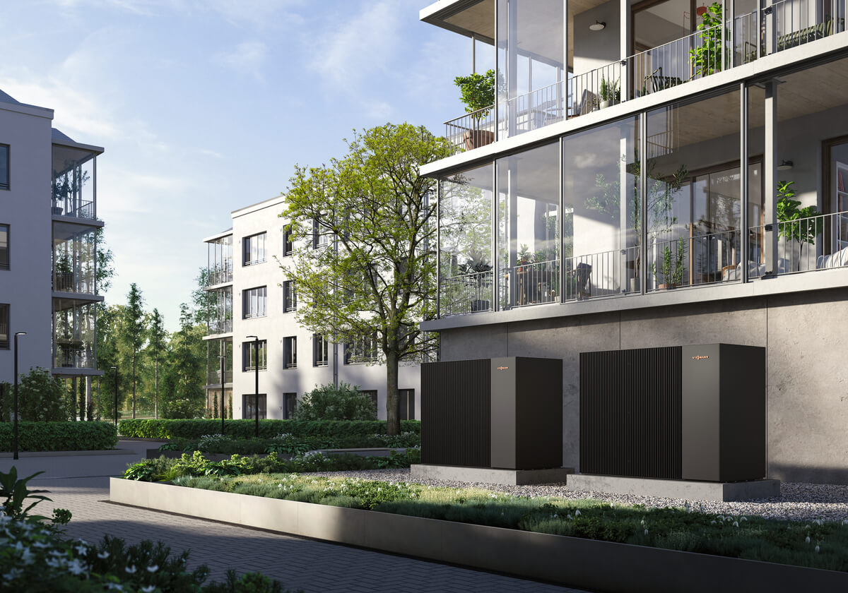 Moderne Wohngebäude im Grünen mit Solaranlagen und eleganten, schwarzen Wärmepumpen im Vordergrund.