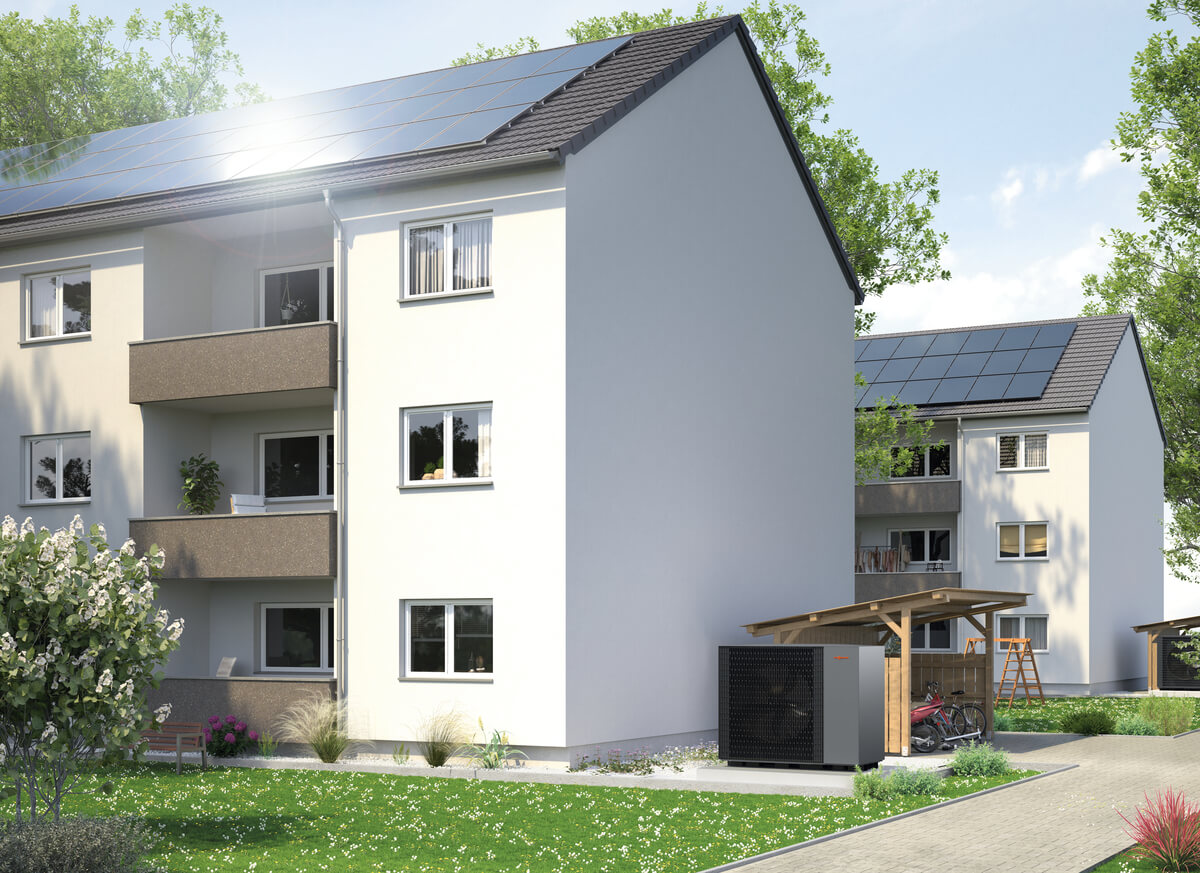 Mehrfamilienhaus mit Solarzellen, helle Fassade, Bäume und blühende Sträucher im Garten.