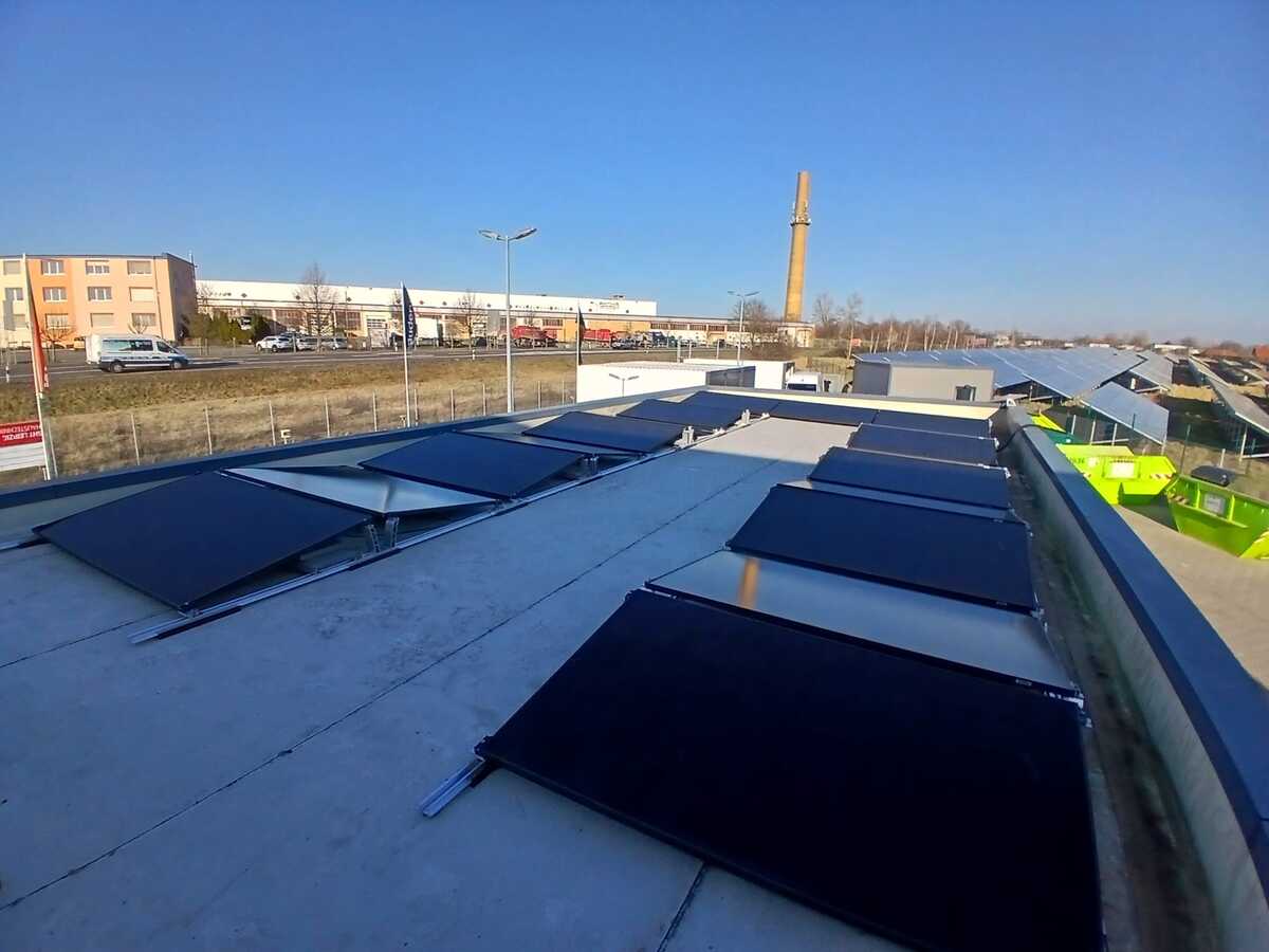 Flaches Dach mit schwarzen Solarpaneelen unter blauem Himmel, gewerbliche Gebäude im Hintergrund.