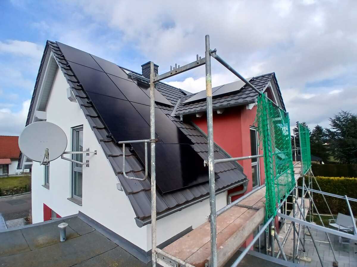 Ein weißes Haus mit roten Akzenten, Solaranlage auf dem Dach und Baugerüst davor.
