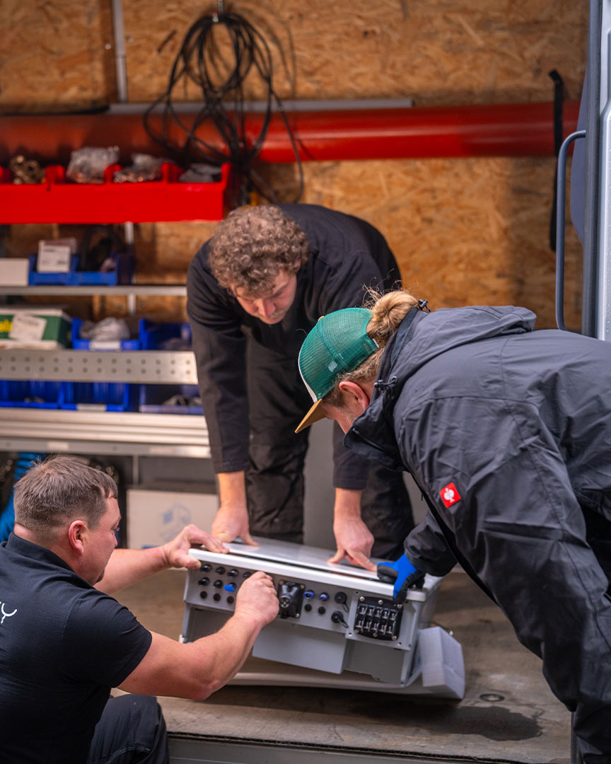 Drei Personen reparieren ein elektronisches Gerät in einer Werkstatt. Sie wirken konzentriert.